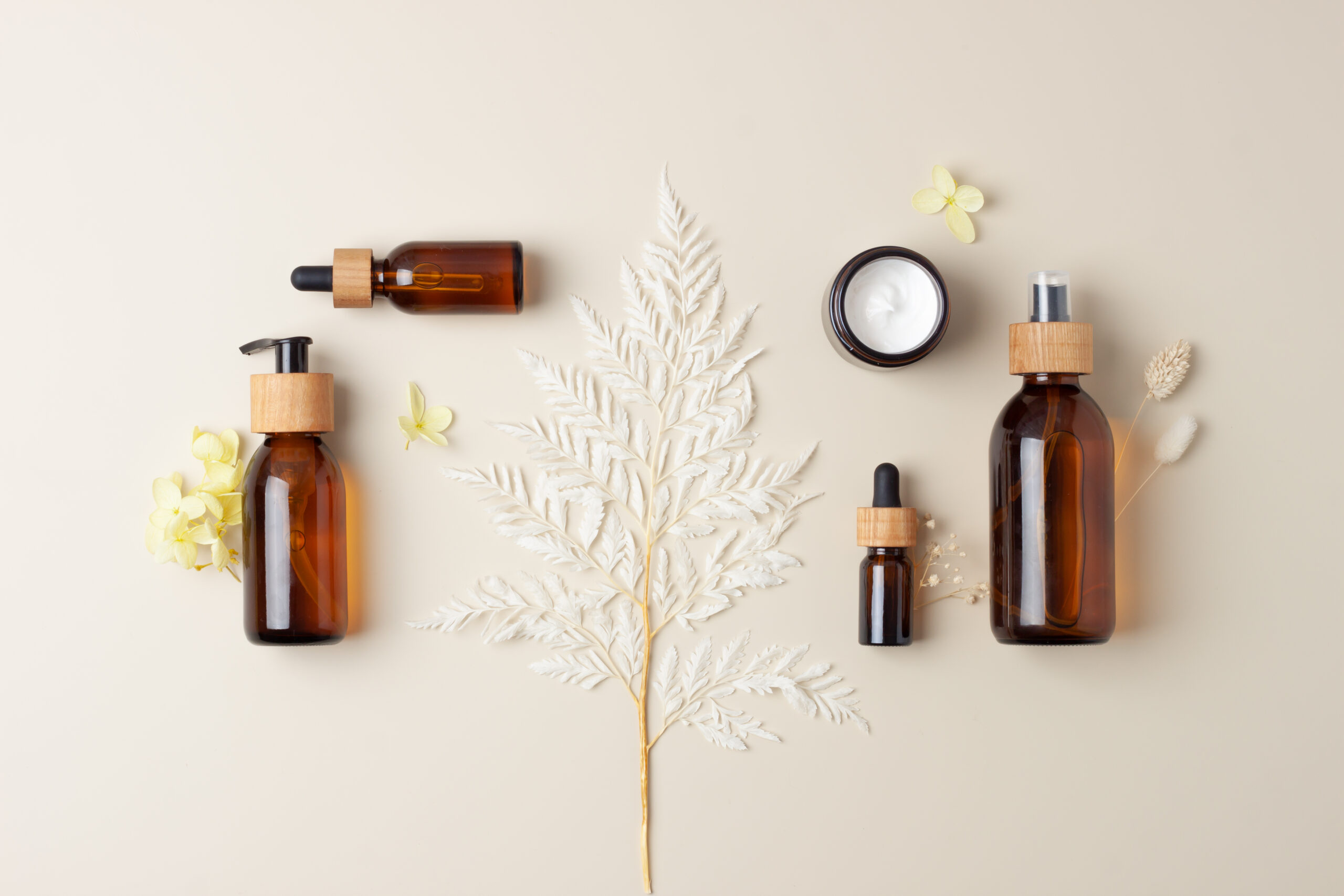Cosmetic composition with cosmetic skin care products and flowers on pastel beige background. Flat lay, copy space